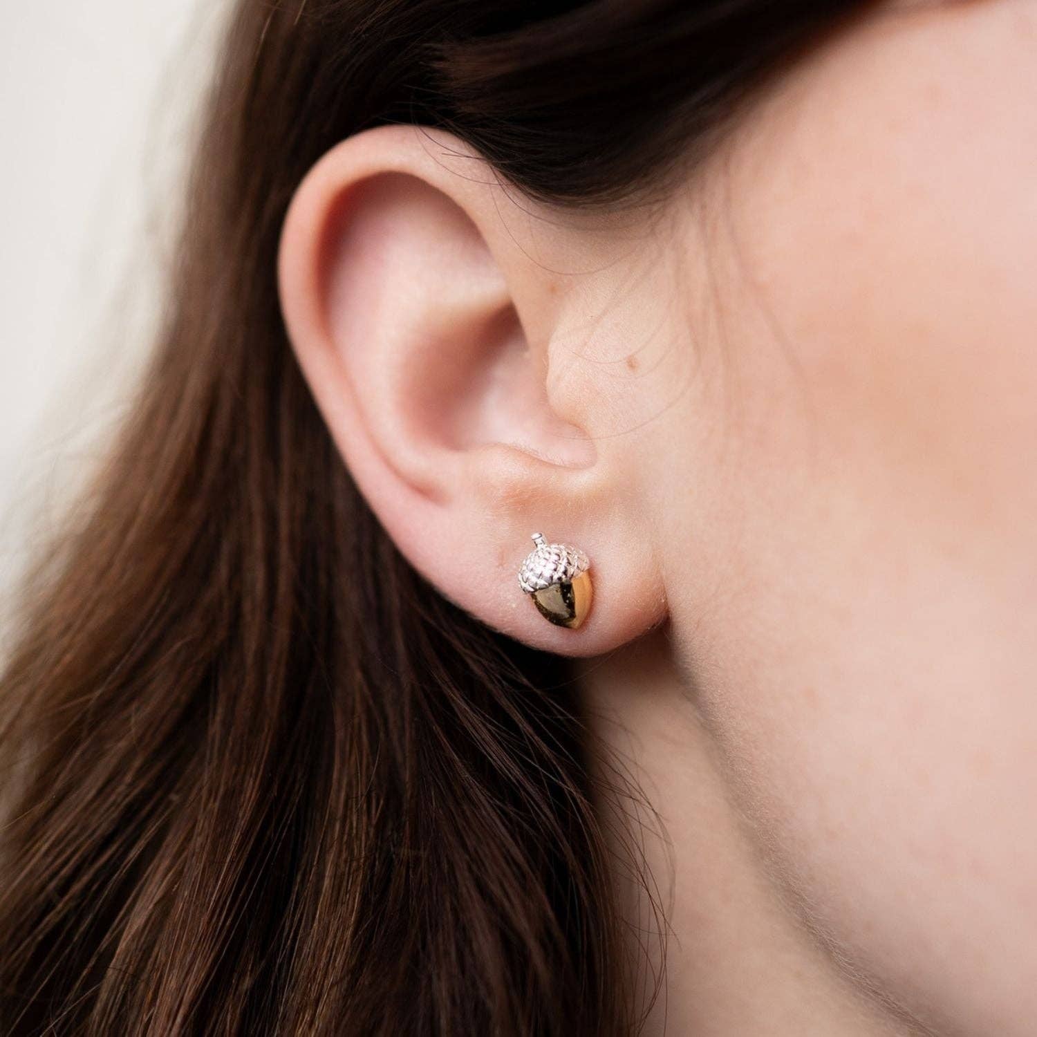 Close-up of an ear wearing a gold and silver earring with a blurred background
